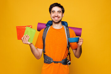 Young traveler man carry backpack with stuff mat hold food snack bowl isolated on plain yellow...
