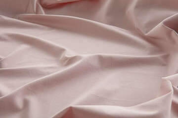 A soft pink fabric lies lightly wrinkled on a flat surface, catching natural light and highlighting its smooth texture and gentle folds, creating a serene atmosphere.