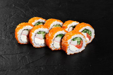 California uramaki rolls covered with tobiko flying fish roe lying on black slate surface