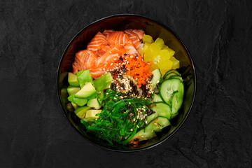 Delicious hawaiian salmon poke bowl with avocado and cucumber on dark background