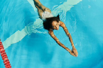 Young woman enjoying a refreshing swim in a sparkling blue pool during summer