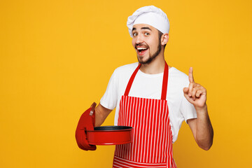 Young housewife housekeeper chef cook baker man wear red apron toque hat hold metal baking form for...
