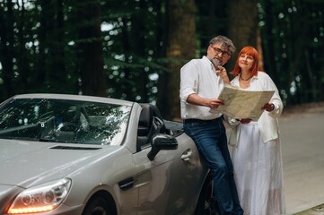 Reading the map. Lovely senior couple standing on the road near convertible cabriolet car