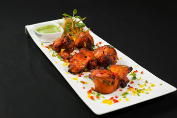 Tandoori Chicken Tikka Boti Kebab on a Platter with Salad and Green Mint Chutney isolated on dark background side view of Pakistani cuisine