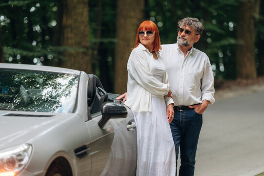 Lovely senior couple standing on the road near convertible cabriolet car