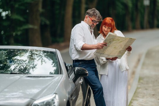 Reading the map. Lovely senior couple standing on the road near convertible cabriolet car