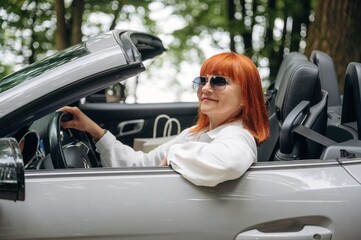 Having great time, in sunglasses. Side view of woman that is driving convertible cabriolet car