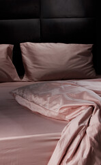 A cozy bed features soft pink sheets and pillows, slightly rumpled, set against a dark wooden...