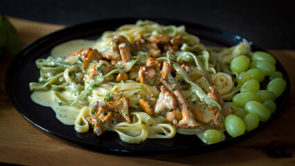 ready to eat - tagliatelle with chanterelles and grapes, served on a black plate on a wood board