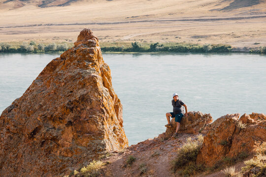 Hiker resting on rocky cliff enjoying view of Ili River flowing through arid landscape in Kazakhstan