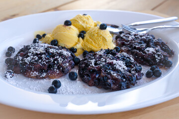 ready to eat - fresh homade tyrolean blueberry pancakes with ice cream, blueberries and powder sugar, served on a white plate