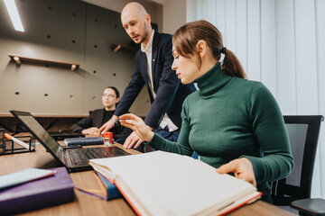 Colleagues collaborate in an office, working on a laptop and engaging with documents, symbolizing...