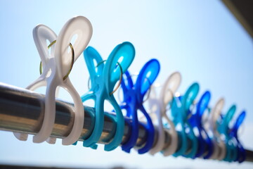 青空の下、物干し竿に並んだ白と青の洗濯ばさみ。シンプルで爽やかな生活の一場面を切り取った日常感あふれる夏らしい写真。