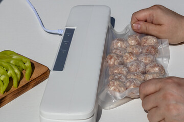 A person sealing food in a vacuum sealer. The device is white and modern. Green apples are on a wooden cutting board nearby. The scene is bright and clean.