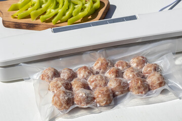 Vacuum-sealed meatballs and green peppers on a white surface. The meatballs are neatly packed in a...