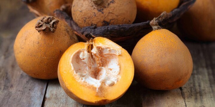 Vibrant calabash fruits, cut and whole, on a rustic wooden table in a close-up shot.
