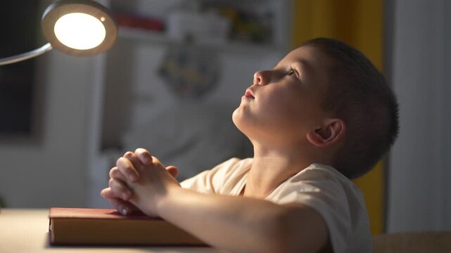 Young boy is praying. Religious leader prays to a child. Book of prayers on a table lifestyle in the evening. A boy is offering a prayer.