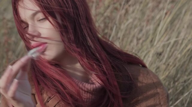 Teen girl in close-up, playfully holding and examining a small fluff, dressed warmly in a cozy autumn landscape.