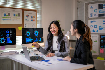Asian businesswomen discussing charts on computer screen in office meeting
