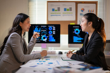 Asian businesswomen discussing charts and data on computer screen in office meeting