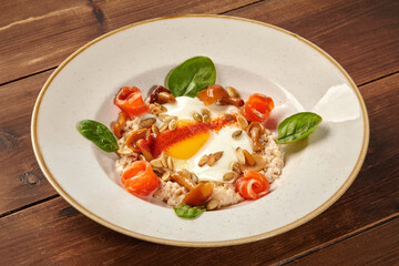 Oatmeal porridge with fried eggs, salmon, mushrooms, and greens on wooden table
