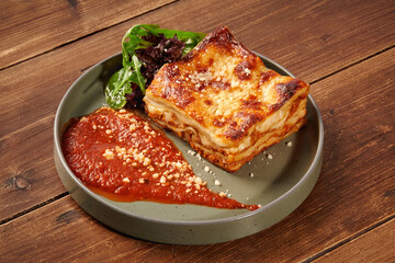 Delicious lasagna bolognese with tomato sauce and parmesan on wooden table