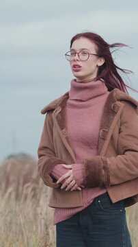 Smiling teenage girl in pink turtleneck sweater and brown shearling coat having a joyful conversation outdoors. Portrait with cloudy sky background. Autumn season and communication concept.