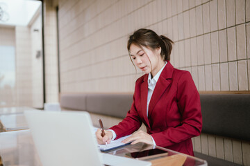 A woman works at a cluttered office desk, reviewing documents and reports. She works with...