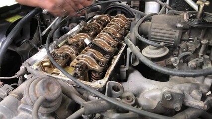 mechanic is conducting a manual tune-up on the rocker arm assembly of a car engine.