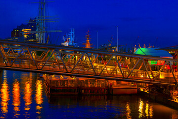 Vibrant night scene of Hamburg harbor, with illuminated ships, modern buildings, and reflections shimmering on the water. Glowing bridge and city lights create a colorful, dynamic urban atmosphere