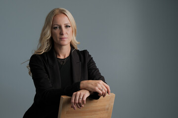 Portrait of a confident business woman wearing black suit sitting on the chair isolated on grey background.