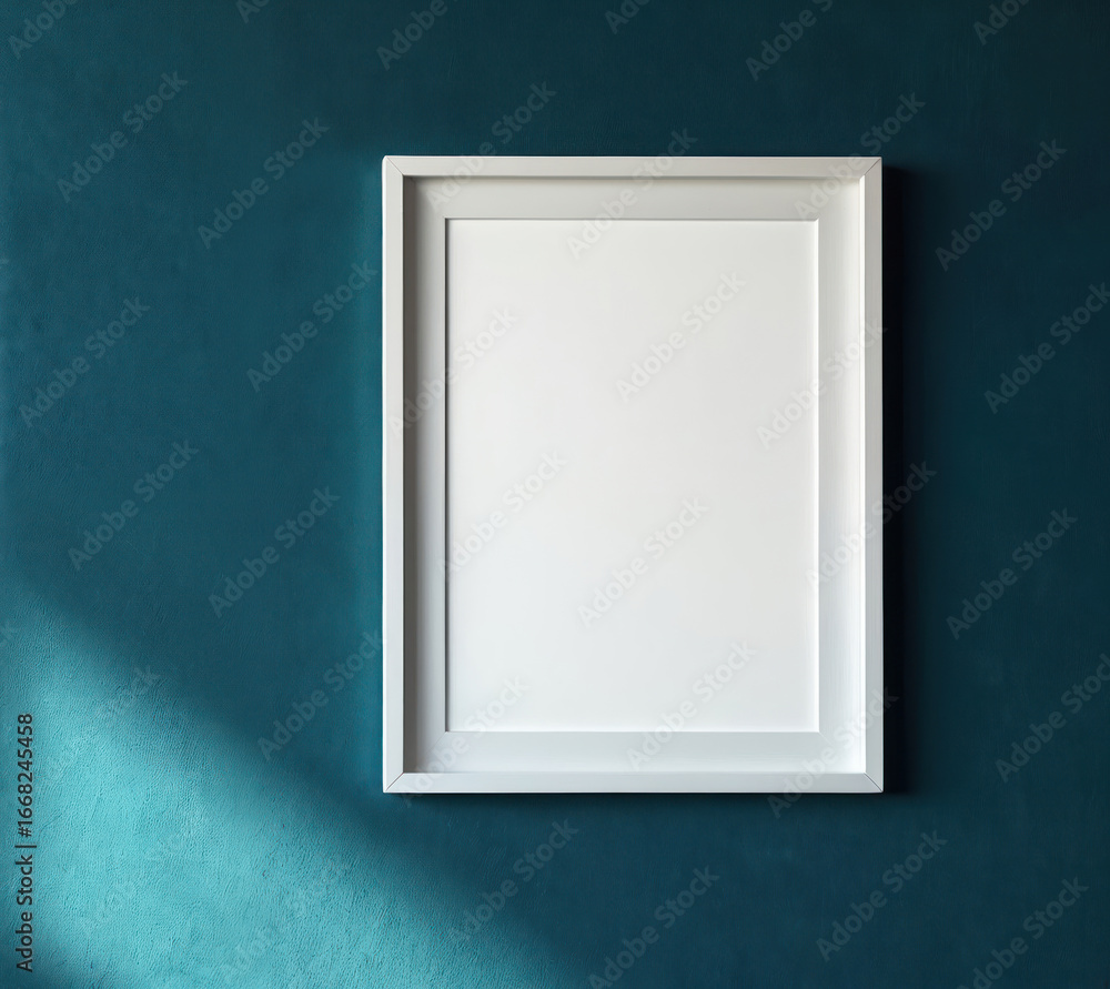 Poster white empty picture frame mounted on deep teal wall. light shadow falls across textured surface, cre