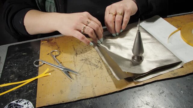 Woman seamstress tears off adhesive tape from layered textile fabric. Careful handwork at table in clothing manufacture factory closeup