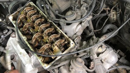 mechanic is conducting a manual tune-up on the rocker arm assembly of a car engine.