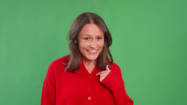 A woman in a red sweater smiling and pointing at herself against a green background