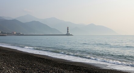 Lighthouse on a pier with waves crashing on a pebble beach and mountains ocean coast