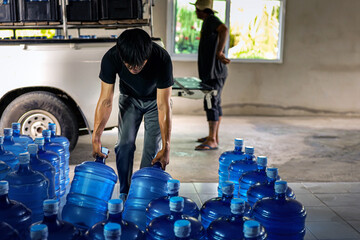 male warehouse worker lifting a Gallon drinking water, Workers transfer drinking water bottles from...