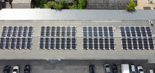 Aerial top view of multiple solar panels mounted on a flat roof of an industrial building for...