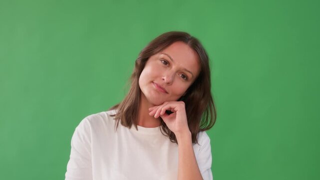 A woman with long brown hair, wearing a white shirt, thoughtfully resting her chin on her hand against a green background