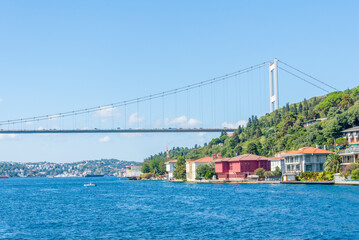 Fototapeta premium Bosphorus Bridge spans a serene waterway with charming waterfront homes in Istanbul on a sunny day