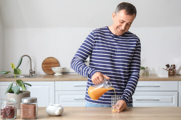 Mature man pouring orange juice into glass in kitchen