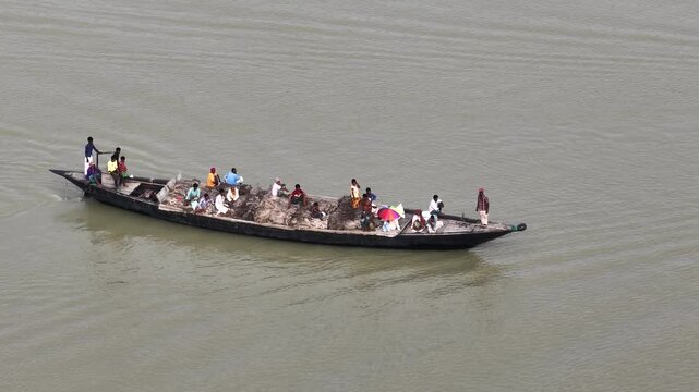 Jamalpur, Bangladesh - 23 August 2025: Aerial view of a long boat filled with people sailing on the river, creating ripples on the water surface.