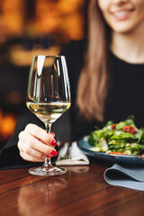 Female diner raising glass of white wine with salad