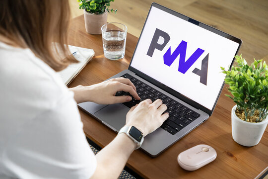 Poznan, Poland - August 23, 2025: Woman actively typing on a modern laptop displaying PWA, symbolizing progressive web application development and efficient remote work culture