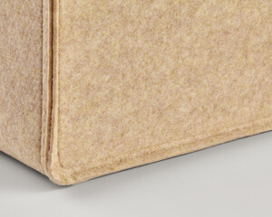 Corner of beige felt bag showing stitching detail on neutral background
