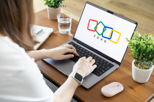 Poznan, Poland - August 23, 2025: Zoho application logo prominently displayed on a laptop, with a person actively typing, highlighting modern remote work and digital business solutions