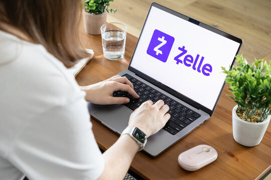 Poznan, Poland - August 23, 2025: Zelle application logo on laptop screen, person typing, showing fast digital money transfers and secure online payment