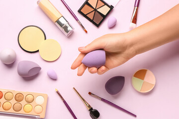 Female hand with makeup sponge and decorative cosmetics on pink background