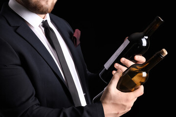 Sommelier holding bottles with different types of wine on black background