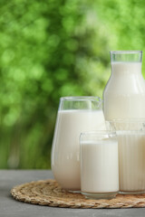 Glasses and bottle of fresh milk on grey table outdoors
